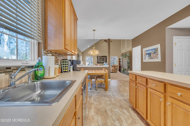 kitchen featuring a sink, an inviting chandelier, vaulted ceiling, light countertops, and backsplash