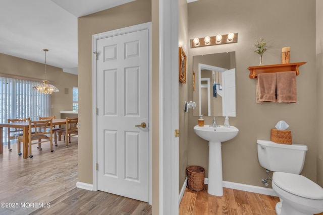 half bathroom featuring toilet, baseboards, a chandelier, and wood finished floors