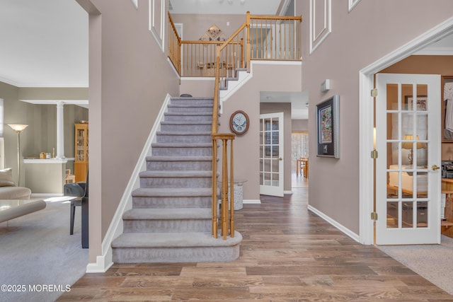 stairway featuring decorative columns, baseboards, a towering ceiling, wood finished floors, and french doors