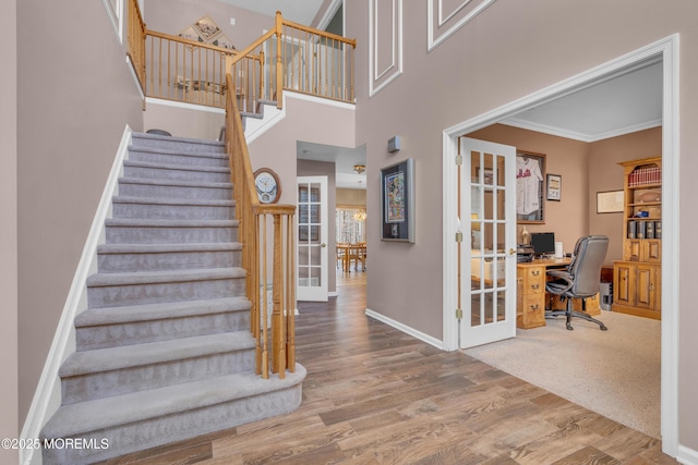 staircase with a high ceiling, wood finished floors, baseboards, french doors, and crown molding