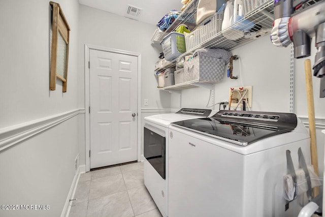 washroom featuring laundry area, washing machine and dryer, visible vents, and light tile patterned flooring