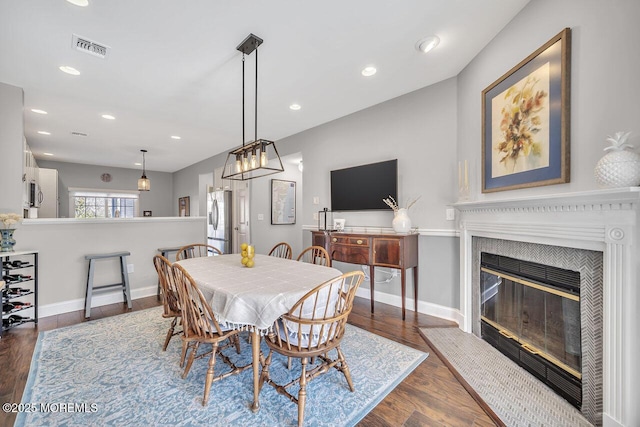 dining space featuring dark wood-style floors, a glass covered fireplace, visible vents, and baseboards