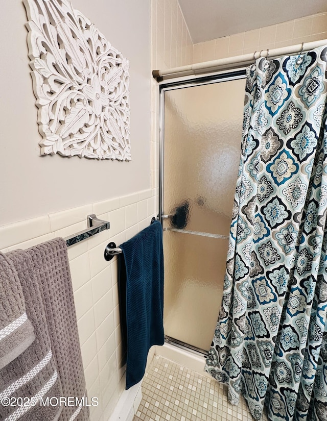 bathroom with tile patterned flooring, a wainscoted wall, tile walls, and a shower stall