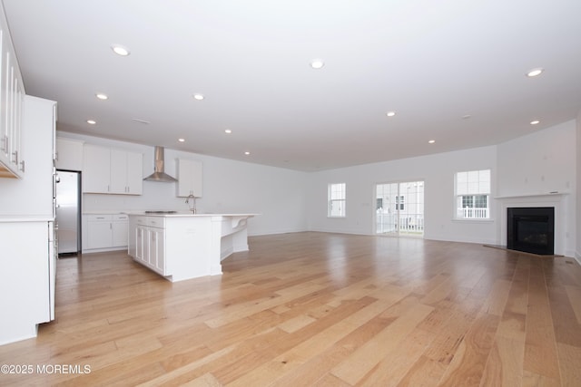 kitchen featuring light wood-style floors, open floor plan, light countertops, freestanding refrigerator, and wall chimney exhaust hood