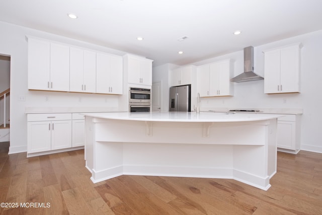 kitchen featuring stainless steel appliances, white cabinets, a spacious island, and wall chimney exhaust hood