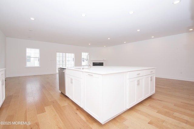 kitchen with open floor plan, a kitchen island with sink, a sink, and light wood-style flooring