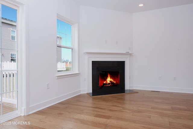 unfurnished living room featuring recessed lighting, visible vents, baseboards, a lit fireplace, and light wood finished floors