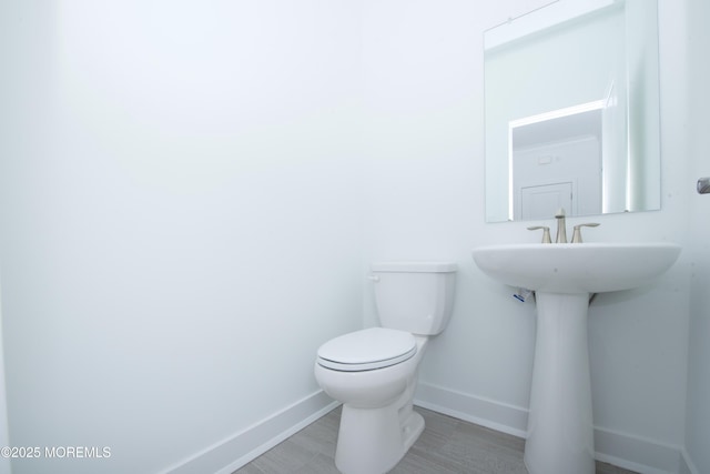 half bathroom featuring toilet, a sink, baseboards, and wood finished floors