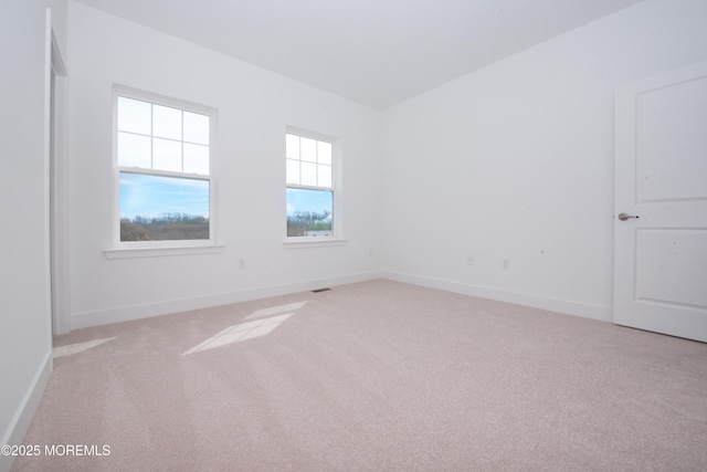 spare room featuring light carpet and baseboards