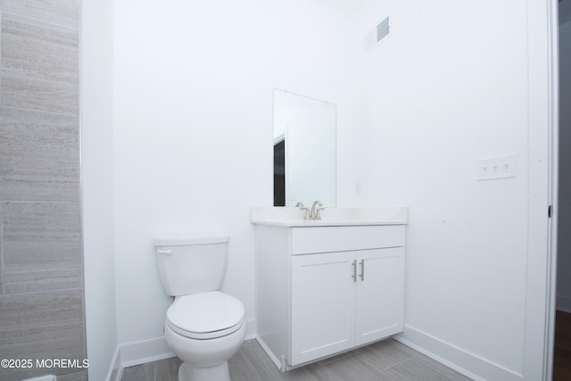 half bath with toilet, baseboards, visible vents, and vanity