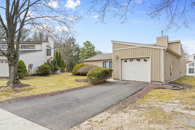 view of side of home with an attached garage, aphalt driveway, and a lawn