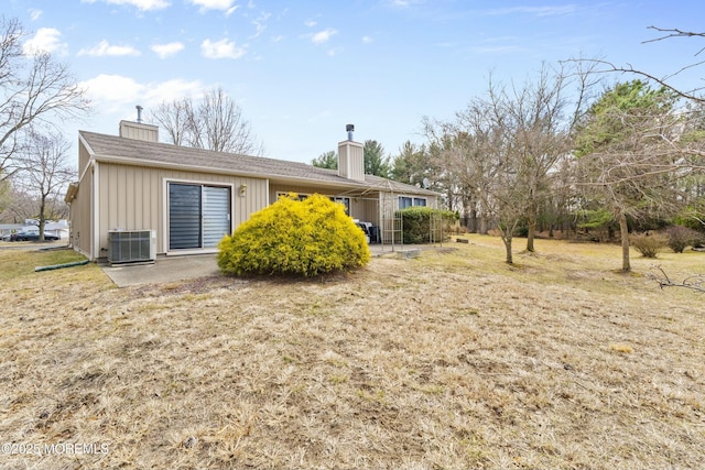 rear view of property with central AC unit, a lawn, a chimney, a patio area, and board and batten siding