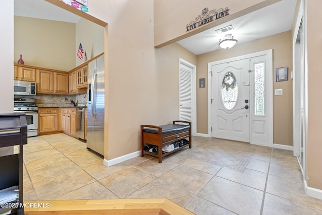 foyer entrance featuring light tile patterned floors, a high ceiling, visible vents, and baseboards