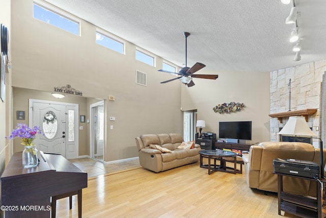 living room with a textured ceiling, ceiling fan, light wood-style flooring, visible vents, and baseboards