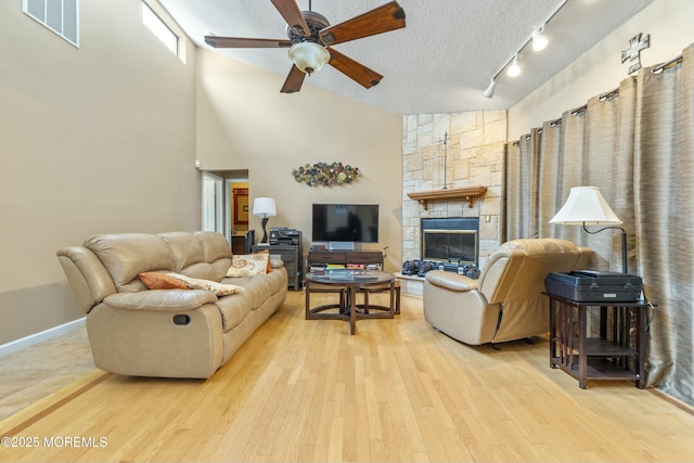 living area featuring a textured ceiling, a stone fireplace, a ceiling fan, visible vents, and light wood-style floors