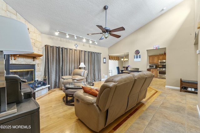 living room with baseboards, a textured ceiling, light wood-type flooring, a fireplace, and ceiling fan with notable chandelier