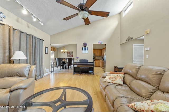 living area with a textured ceiling, lofted ceiling, light wood-style flooring, ceiling fan with notable chandelier, and rail lighting