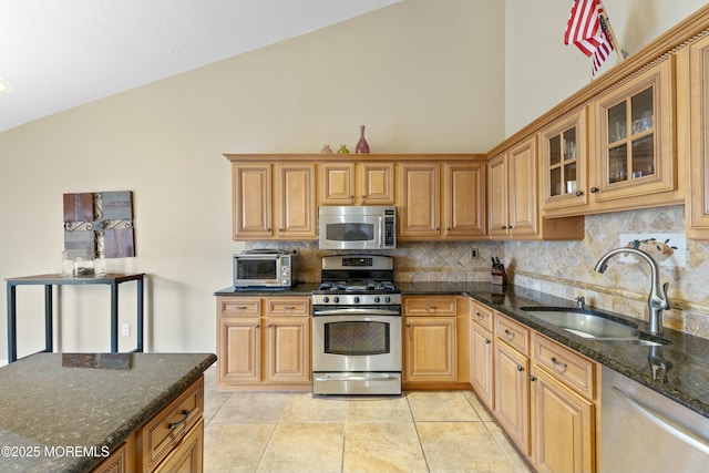 kitchen featuring stainless steel appliances, a sink, tasteful backsplash, dark stone countertops, and glass insert cabinets