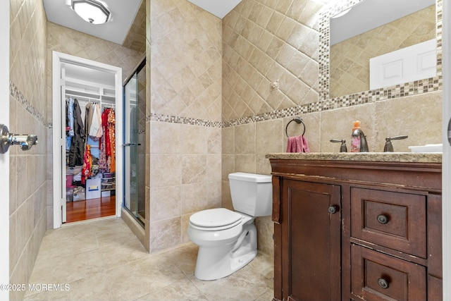 full bathroom with tile walls, toilet, a stall shower, vanity, and tile patterned flooring