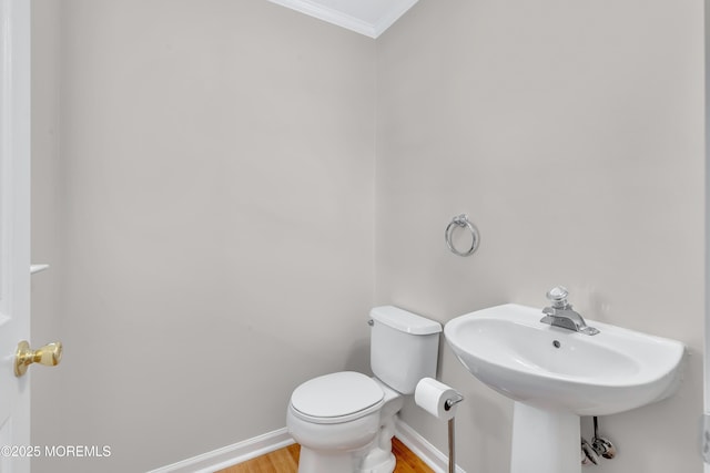 bathroom with crown molding, toilet, a sink, wood finished floors, and baseboards