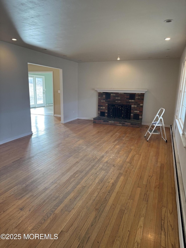 unfurnished living room featuring baseboards, hardwood / wood-style flooring, a baseboard radiator, a brick fireplace, and recessed lighting