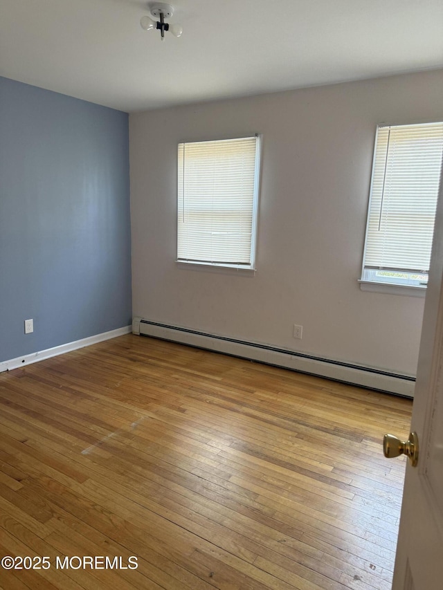 empty room with a baseboard radiator, baseboards, and hardwood / wood-style floors