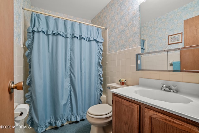 bathroom with wallpapered walls, toilet, shower / tub combo with curtain, vanity, and tile walls