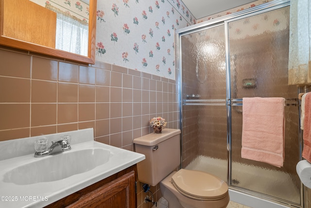 bathroom with toilet, tile walls, wainscoting, a stall shower, and wallpapered walls