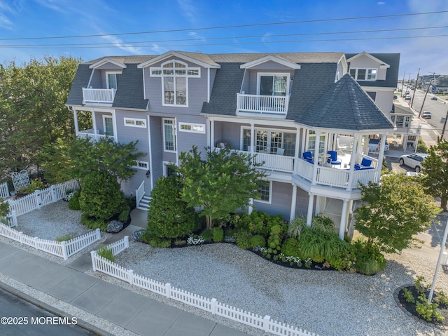 view of front of property with a balcony, roof with shingles, fence private yard, and a gate