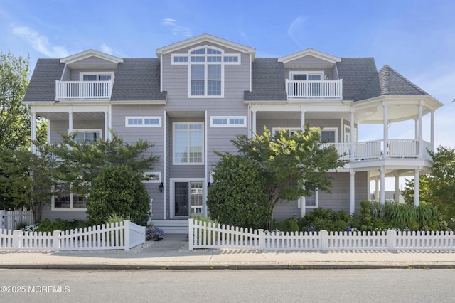 view of front of house featuring a shingled roof, a fenced front yard, and a balcony