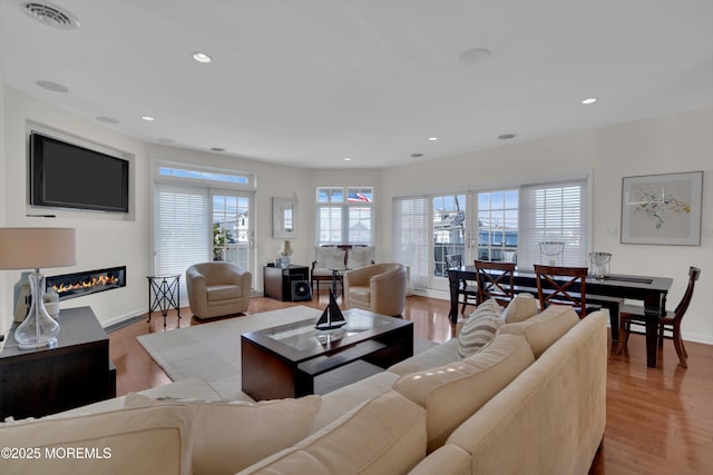 living room featuring recessed lighting, wood finished floors, visible vents, baseboards, and a glass covered fireplace