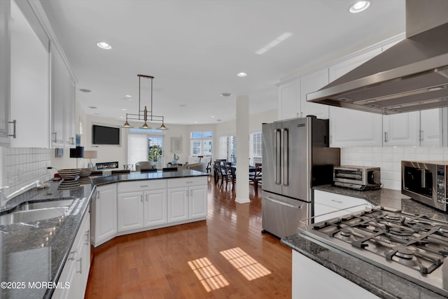 kitchen featuring light wood-style flooring, stainless steel appliances, a peninsula, white cabinetry, and ventilation hood