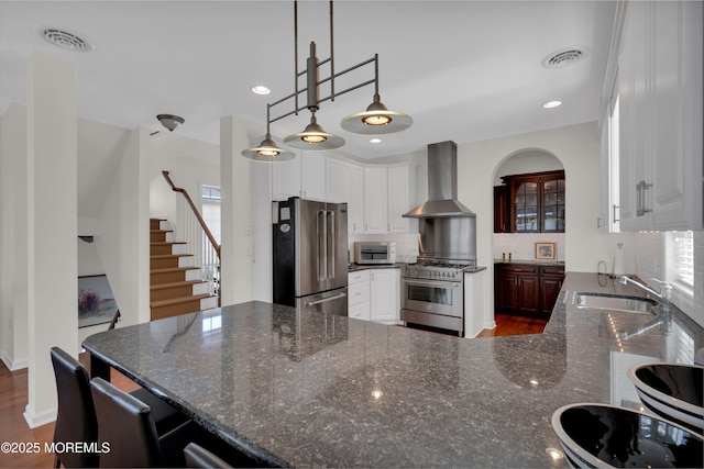 kitchen with wall chimney range hood, high quality appliances, visible vents, and a sink