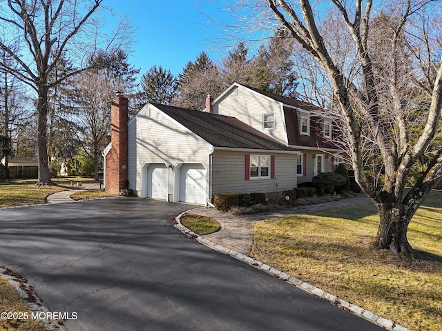 view of front of house with a garage, a gambrel roof, driveway, a front lawn, and a chimney