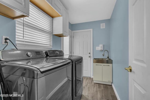 laundry room featuring a sink, baseboards, light wood-style floors, independent washer and dryer, and cabinet space