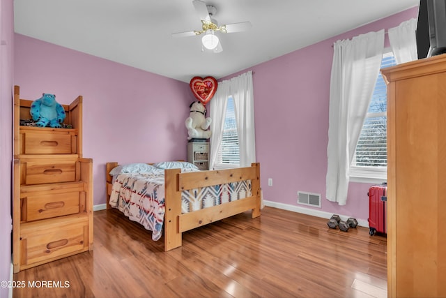 bedroom with a ceiling fan, wood finished floors, visible vents, and baseboards