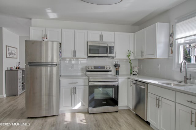 kitchen with white cabinets, stainless steel appliances, a sink, and light countertops