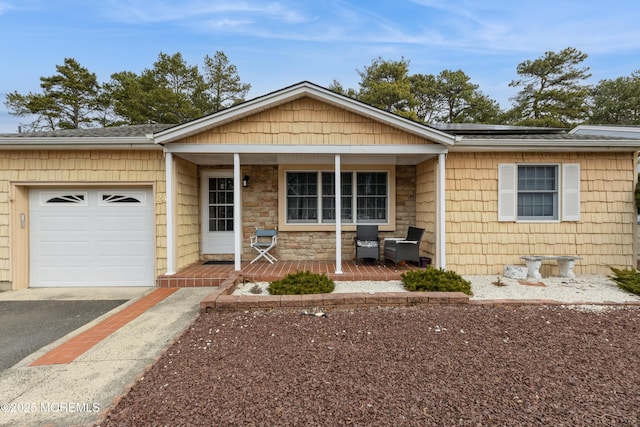 single story home with aphalt driveway, solar panels, a porch, a garage, and stone siding