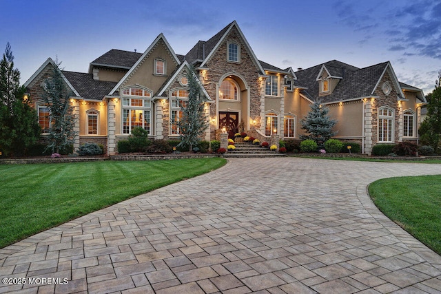 view of front facade with a front yard, stone siding, driveway, and stucco siding