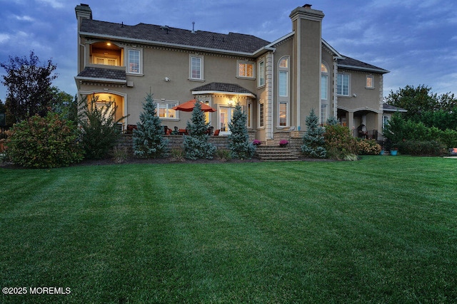 rear view of house featuring stucco siding, a yard, and a chimney