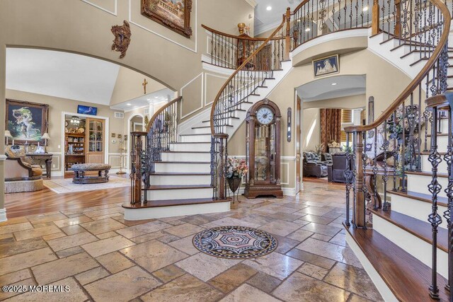 foyer with stone tile floors, recessed lighting, stairway, arched walkways, and a towering ceiling