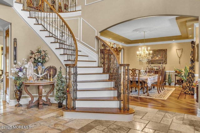 stairs with stone tile floors, a raised ceiling, an inviting chandelier, and ornamental molding