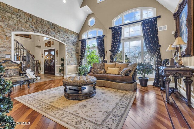 living room with hardwood / wood-style floors, arched walkways, visible vents, and high vaulted ceiling