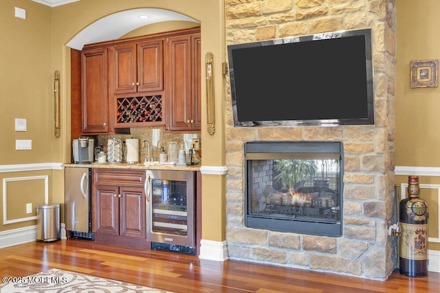 bar featuring stainless steel refrigerator, backsplash, wood finished floors, wine cooler, and indoor wet bar