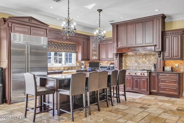 kitchen featuring stainless steel built in refrigerator, a sink, stone tile floors, a breakfast bar area, and crown molding