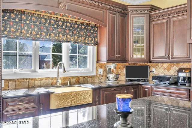 kitchen with decorative backsplash, dark stone counters, glass insert cabinets, and a sink