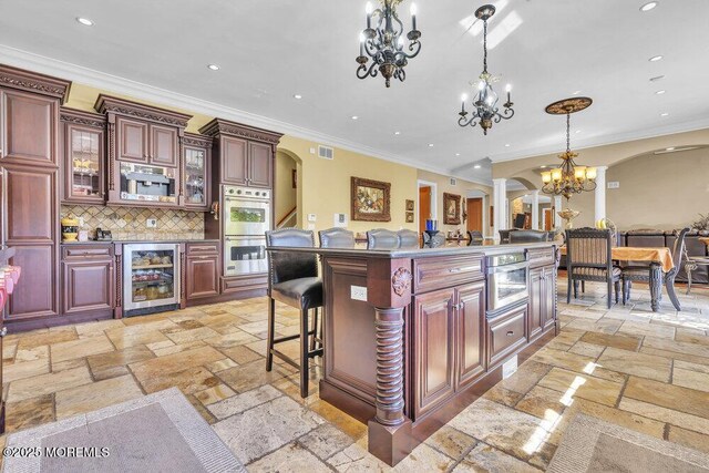 kitchen with stone tile floors, stainless steel double oven, wine cooler, arched walkways, and an inviting chandelier