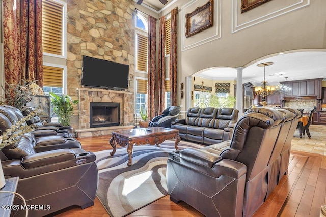 living area with a stone fireplace, an inviting chandelier, wood finished floors, arched walkways, and ornate columns