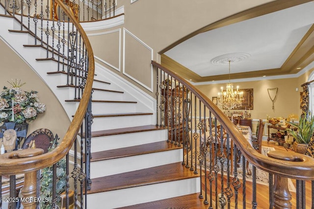 staircase featuring crown molding, a tray ceiling, an inviting chandelier, and wood finished floors