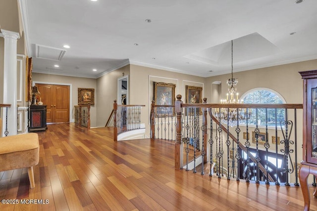 corridor with wood finished floors, attic access, crown molding, a notable chandelier, and an upstairs landing